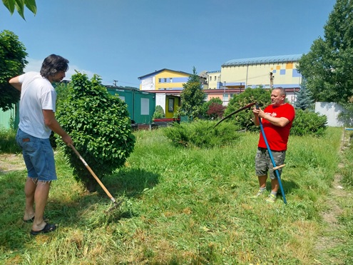 Vľavo dobrovoľník s hrabľami a pri ňom pracovník Domova sv. Jána z Boha s kosou-takto vyzeralo nasadenie za krášlenie záhrady.